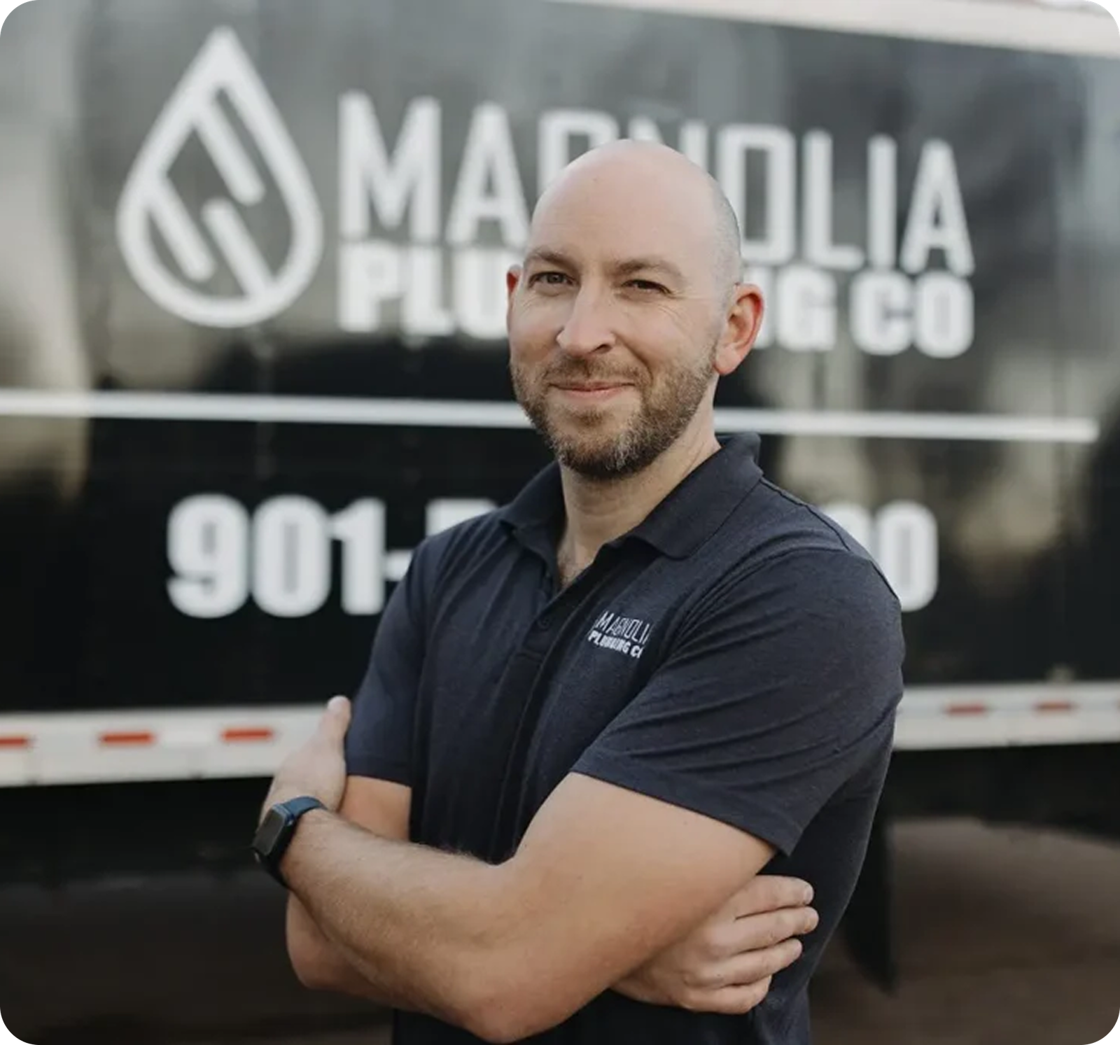 A bearded man stands with arms crossed in front of a Magnolia Plumbing Co. truck in Memphis, TN, wearing a dark polo shirt featuring the Magnolia Plumbing logo.