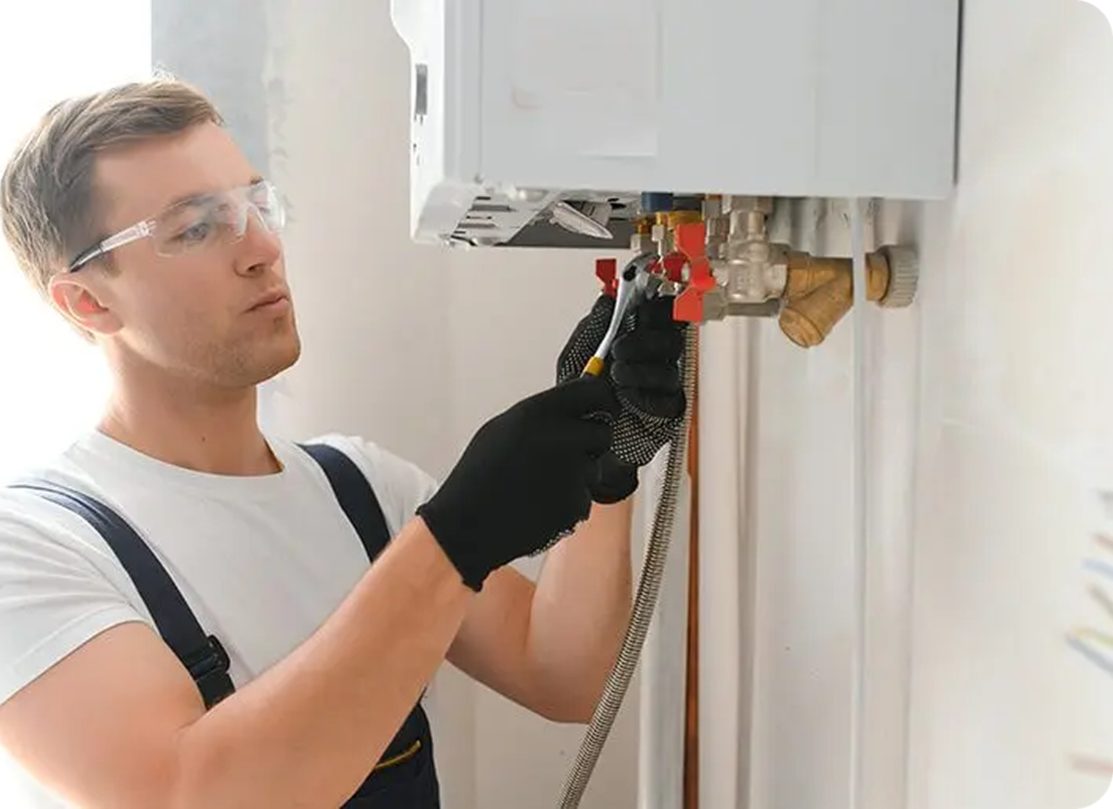 A man wearing safety glasses and black gloves uses a tool to adjust pipes connected to a white wall-mounted boiler, showcasing expert residential plumbing work in Memphis, TN.